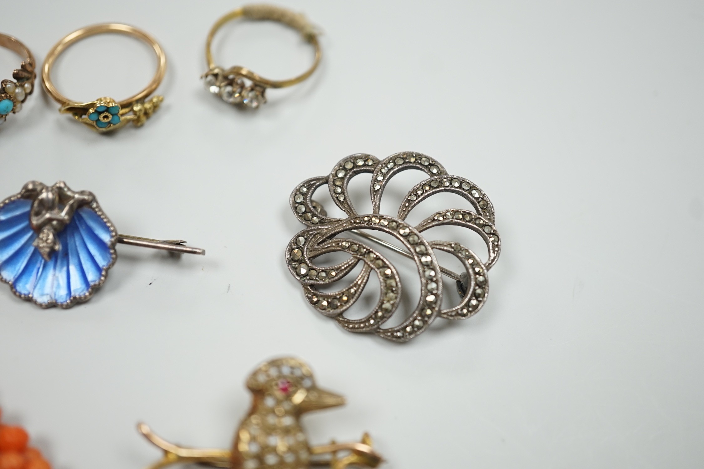A yellow metal, seed pearl and red stone set 'bird on a branch' brooch, width 30mm, two coral bead necklaces, an enamelled white metal imp and shell brooch, three rings, a marcasite brooch and a simulated pearl necklace.